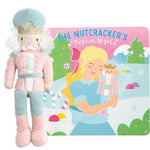 A plush nutcracker doll standing beside a matching illustrated book titled "The Nutcracker's Magical Night," showing a snowy scene with a girl holding the nutcracker. The product is photographed on a clean white background.