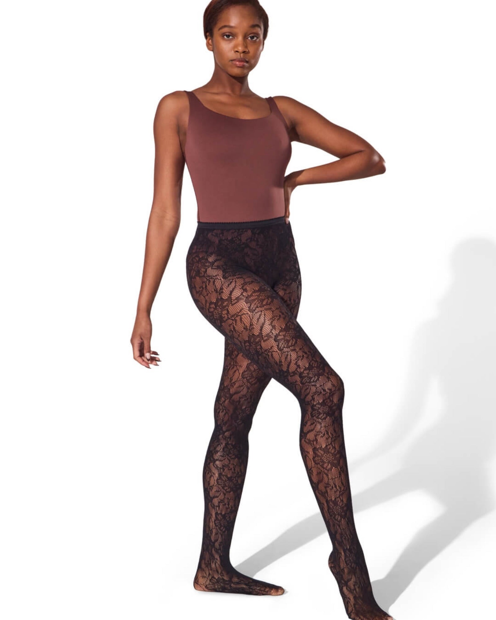 Model wearing brown bodysuit and black lace tights on a white background