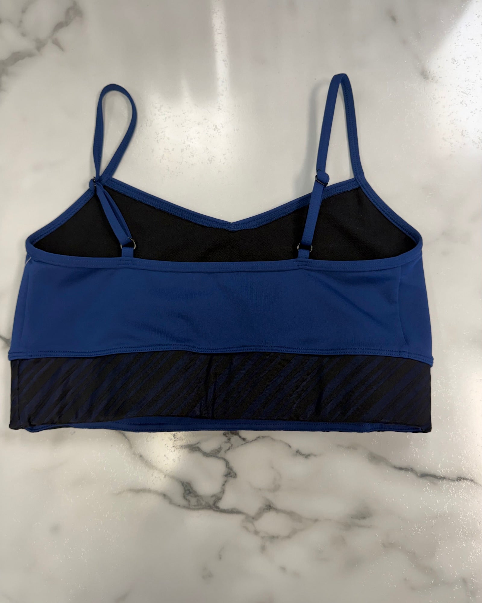 A blue and black dance bra laid flat on a white marble surface.