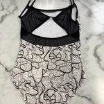 A leotard with a black mesh bustier-style top and a white lower body covered in a black abstract line pattern, laid flat on a white and gray marble surface.