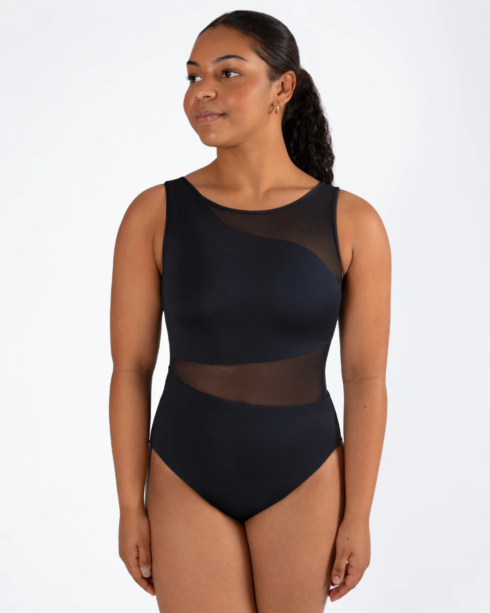 A woman modeling a black sleeveless leotard with sheer mesh panels on the shoulders and waist, set against a plain white studio background.