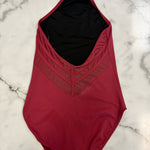A burgundy leotard with a black interior lining, laid flat on a white marble surface.