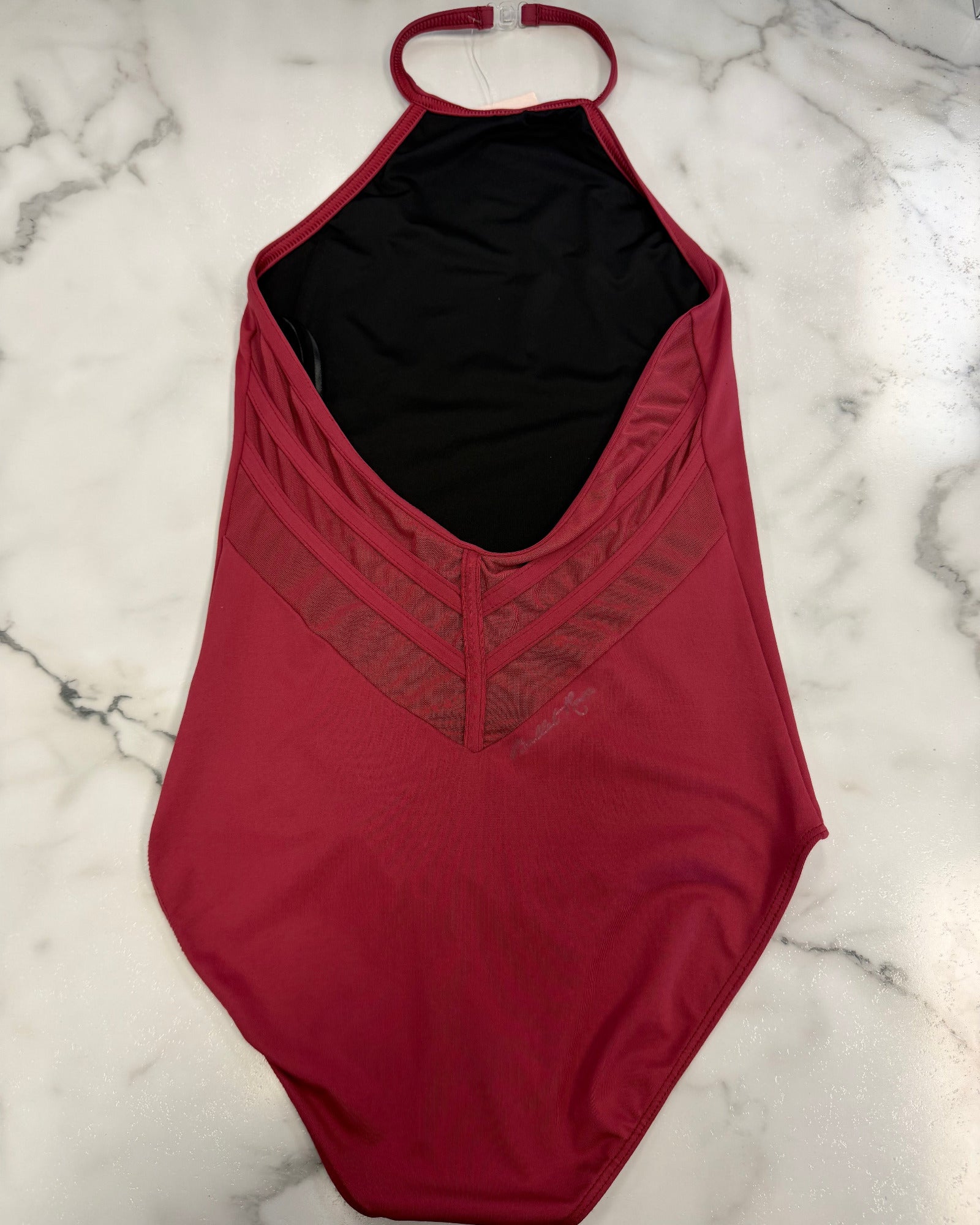A burgundy leotard with a black interior lining, laid flat on a white marble surface.