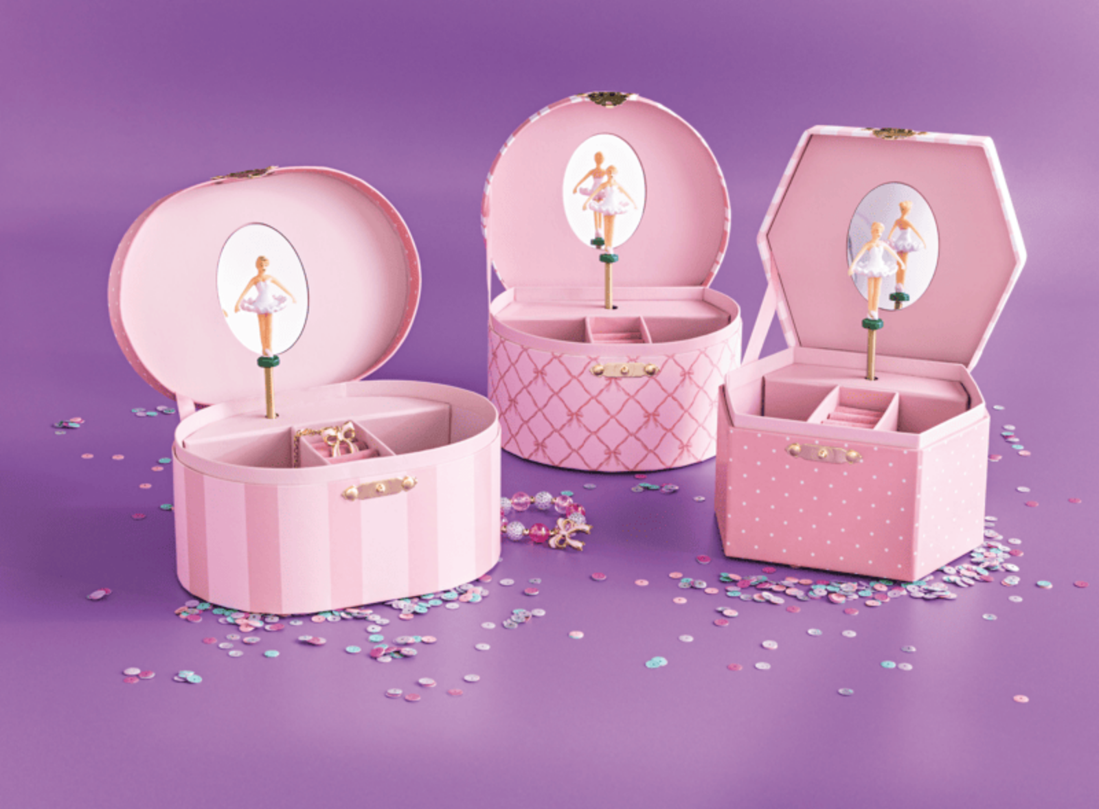 Three pink decorative storage boxes with hinged lids, each featuring a mirror and ballerina illustration, arranged on a purple surface with scattered confetti.