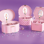 Three pink decorative storage boxes with hinged lids, each featuring a mirror and ballerina illustration, arranged on a purple surface with scattered confetti.