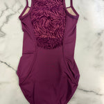 A women's leotard in a deep magenta-purple color, featuring a textured patterned panel on the back and thin shoulder straps, laid flat on a white marble surface.