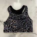 A sleeveless crop top with an iridescent leopard print pattern on a black background, laid flat on a white marble surface.