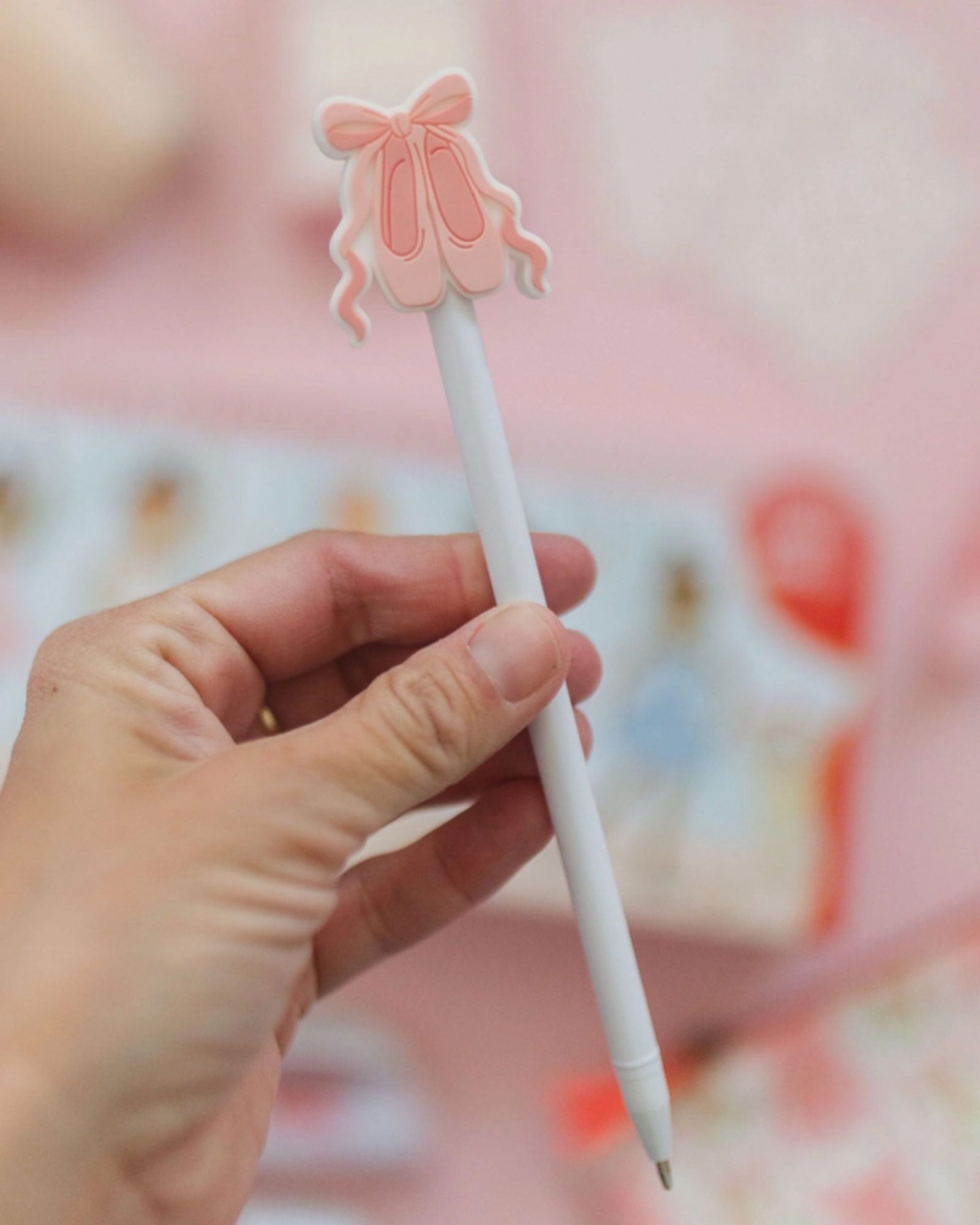 Hand holding a white pen with a pink ballerina clip against a blurred background