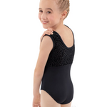 A young girl with blonde braided hair is shown from the back wearing a black sleeveless leotard with a textured lace-like pattern across the upper back and shoulders, set against a plain white background.