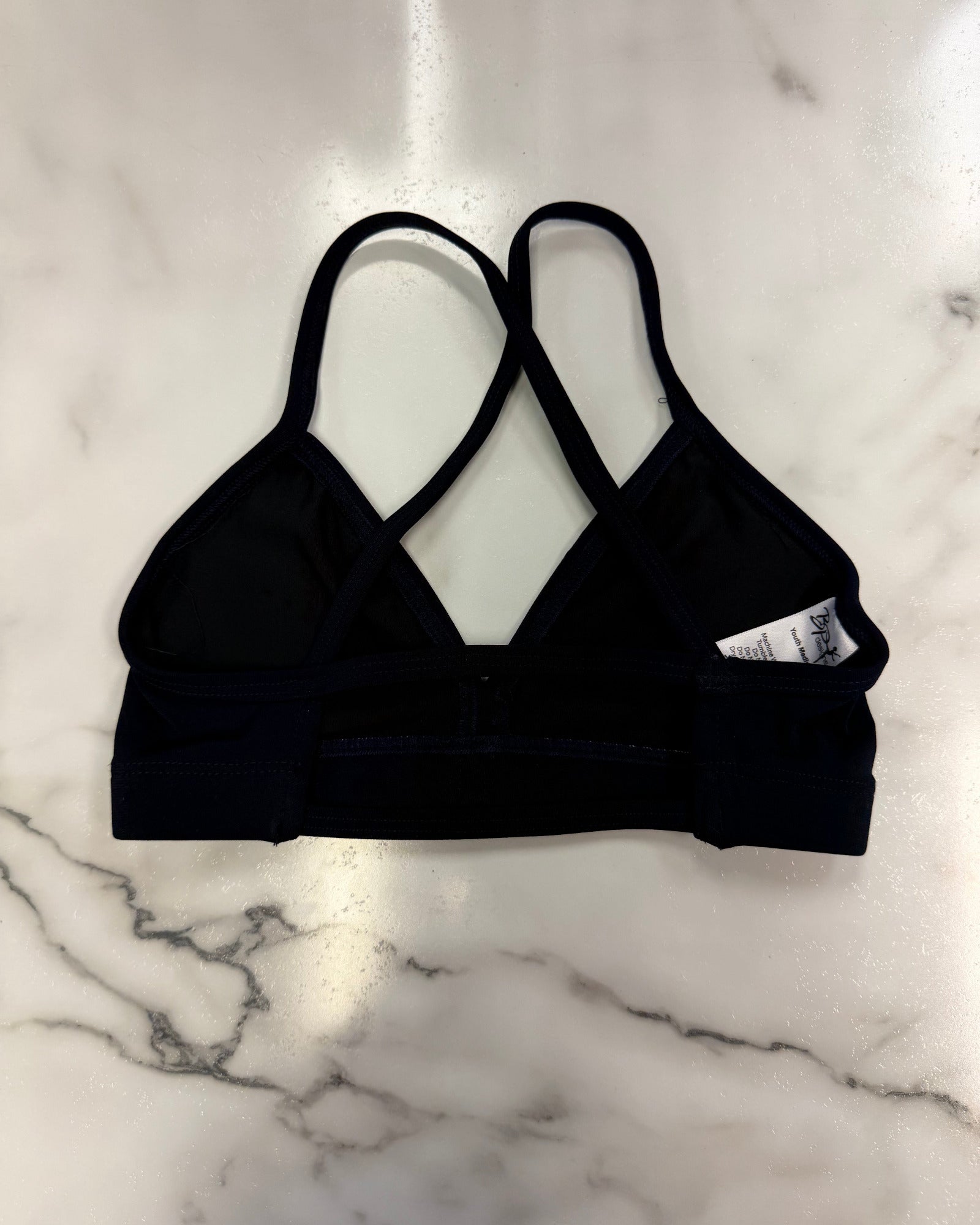 A navy dance bra with crossover straps, laid flat on a white marble surface.
