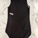 A black sleeveless leotard laid flat on a white marble surface, showing the back view with a textured dotted panel and a small white label.