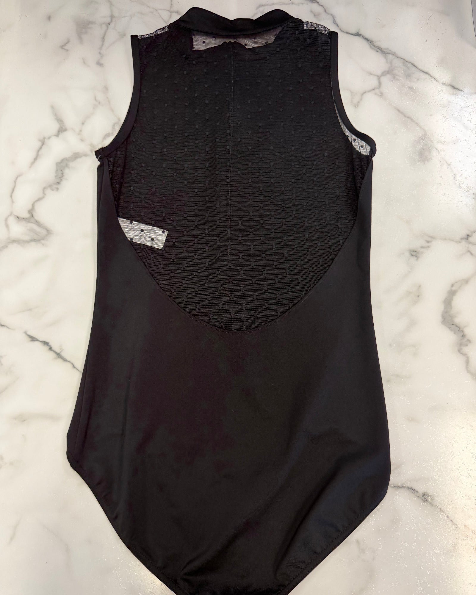 A black sleeveless leotard laid flat on a white marble surface, showing the back view with a textured dotted panel and a small white label.