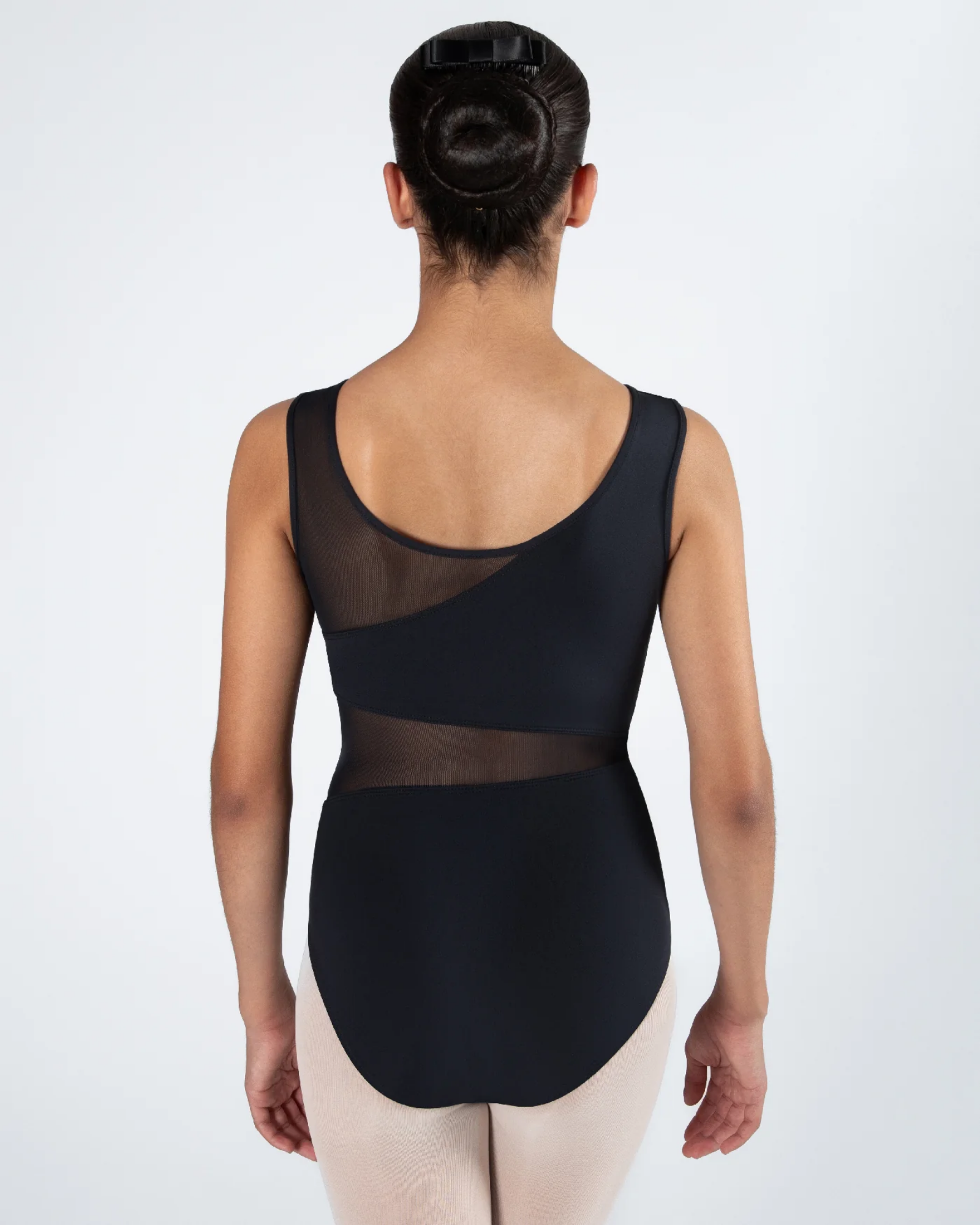 A dancer viewed from the back wearing a black sleeveless leotard with sheer mesh panels and light beige tights, set against a plain light gray studio background.