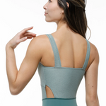 A woman shown from the back wearing a sage green leotard with wide shoulder straps and a side cutout, photographed against a clean white background.