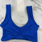A bright royal blue dance bra with a ruched front detail, laid flat on a white marble surface.