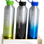 Three aluminum water bottles with gradient finishes in green, black, and blue, each with a matching colored loop cap and the brand name 'CAPEZIO' printed vertically, displayed on a gold-colored metal stand against a white background.