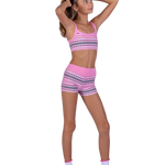 A young girl modeling a pink two-piece dance set with a geometric pattern, consisting of a sports bra and matching shorts, against a plain white background.