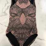 A sleeveless leotard with a pink and black floral lace pattern, laid flat on a white marble surface.