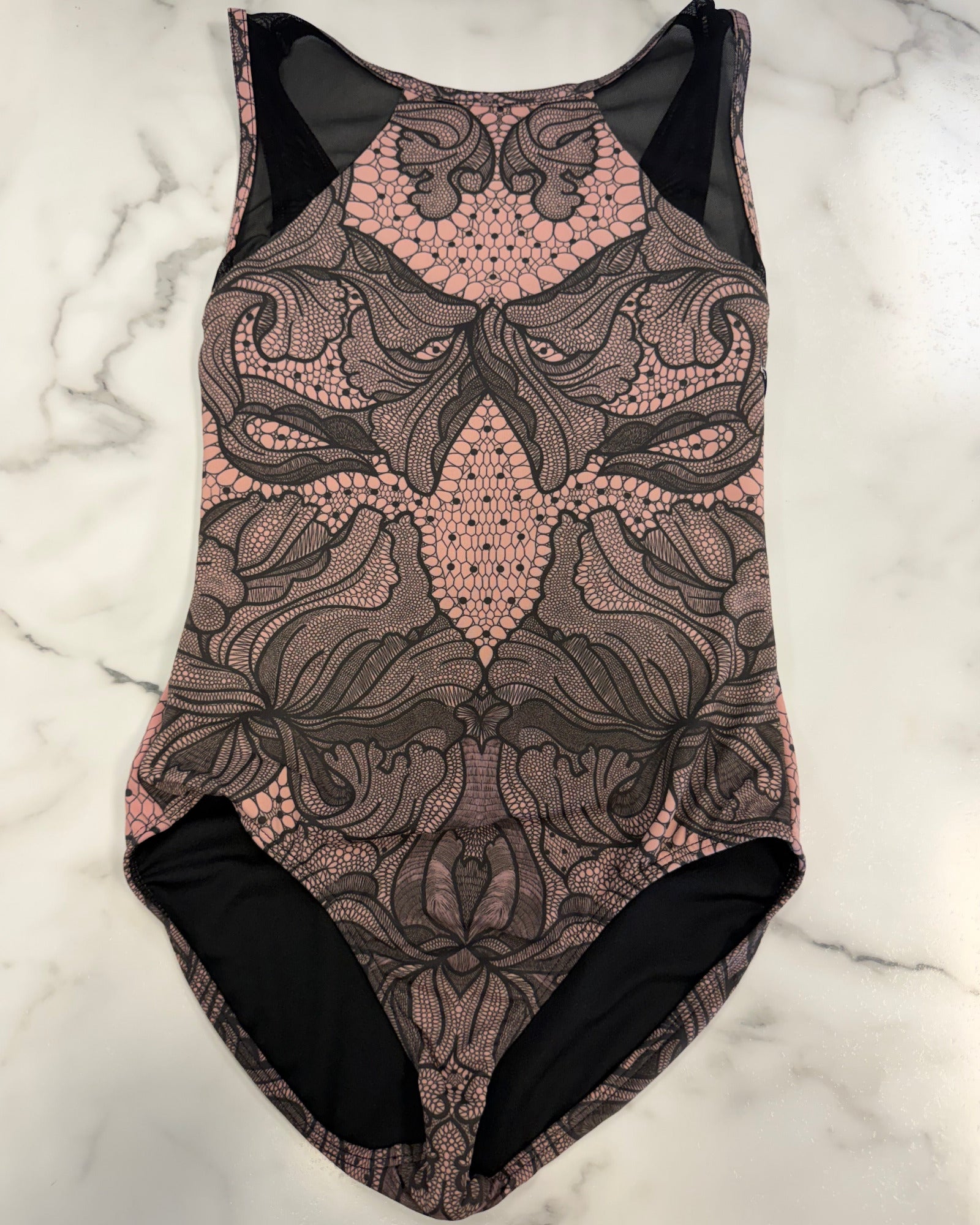 A sleeveless leotard with a pink and black floral lace pattern, laid flat on a white marble surface.