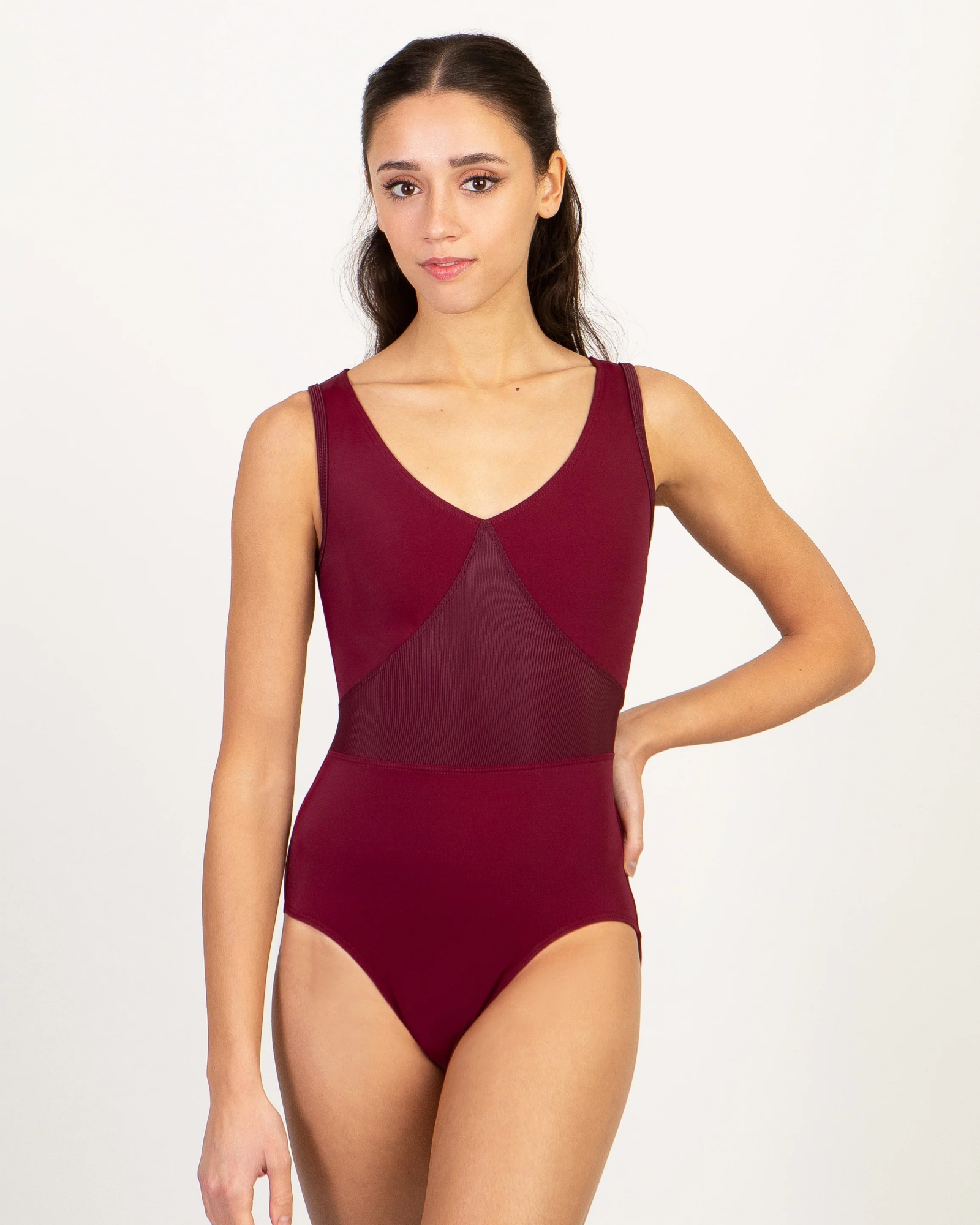 A woman modeling a sleeveless burgundy leotard with a V-neckline and sheer mesh paneling, set against a plain white studio background.