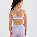 A woman shown from the back wearing a lavender and white two-piece dance set, consisting of a sports bra with crisscross straps and matching high-waisted shorts, against a plain white studio background.