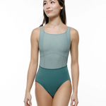 A woman modeling a leotard with a scoop-neck top in sage green and matching  bottom in green, set against a plain white studio background.