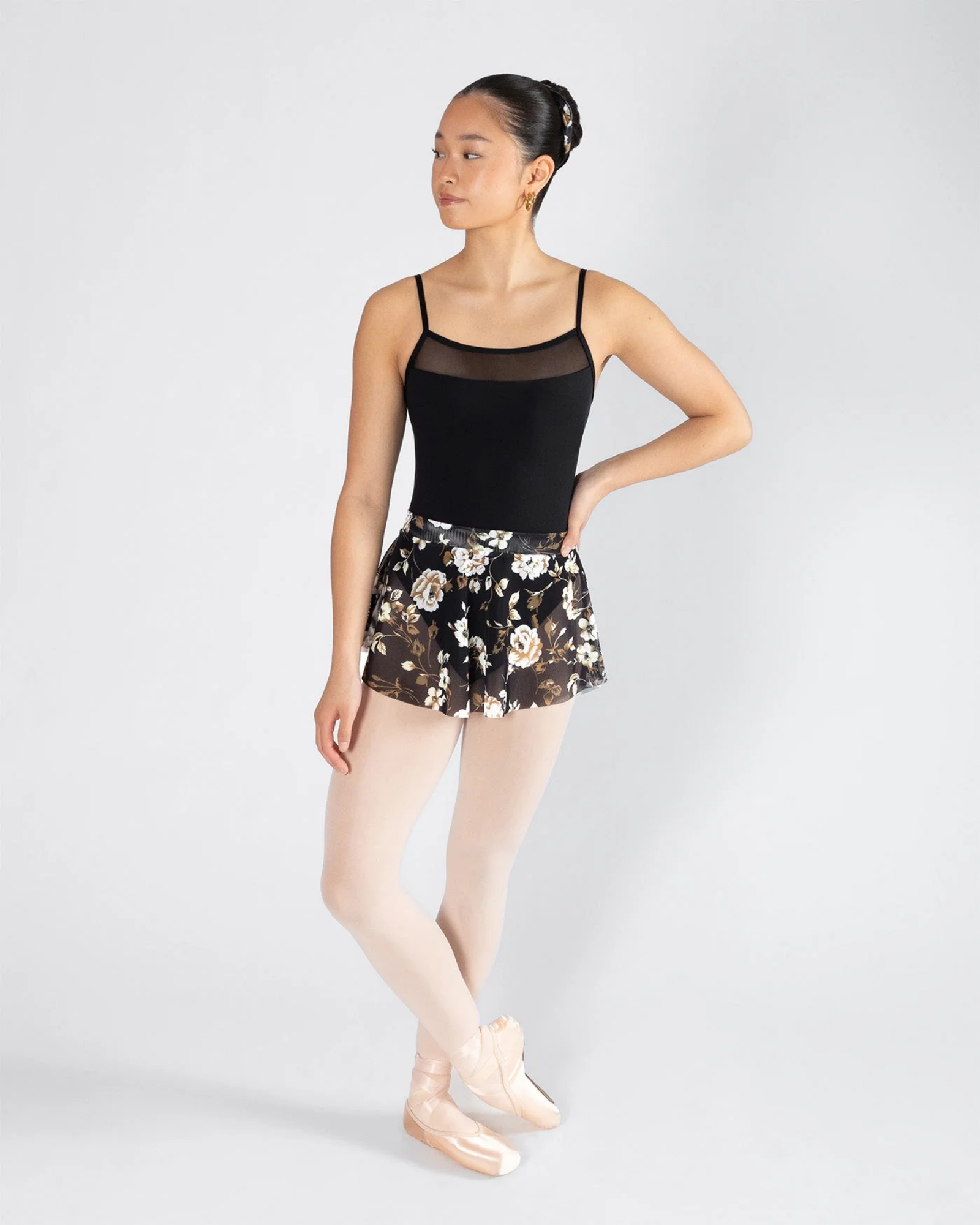 Dancer wearing a black leotard and floral skirt on a white background