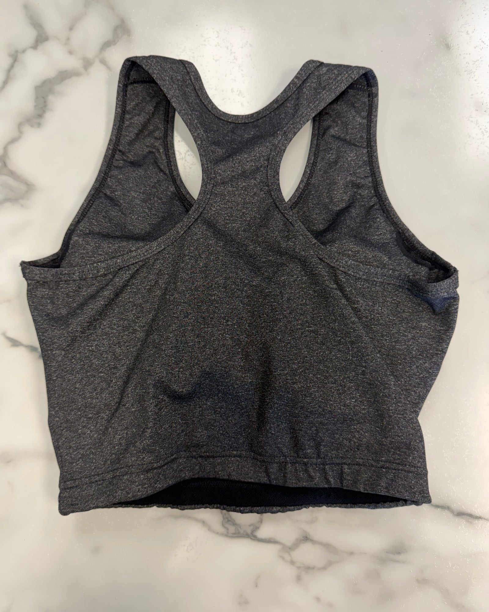 A dark gray heather racerback sports bra laid flat on a white marble surface.