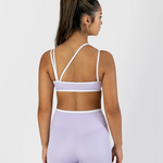 A woman shown from the back wearing a light lavender two-piece dance set with white trim, consisting of a sports bra and high-waisted shorts, against a plain light gray background.