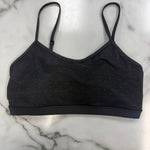 A black bra top with a subtle dotted pattern, laid flat on a white marble surface.