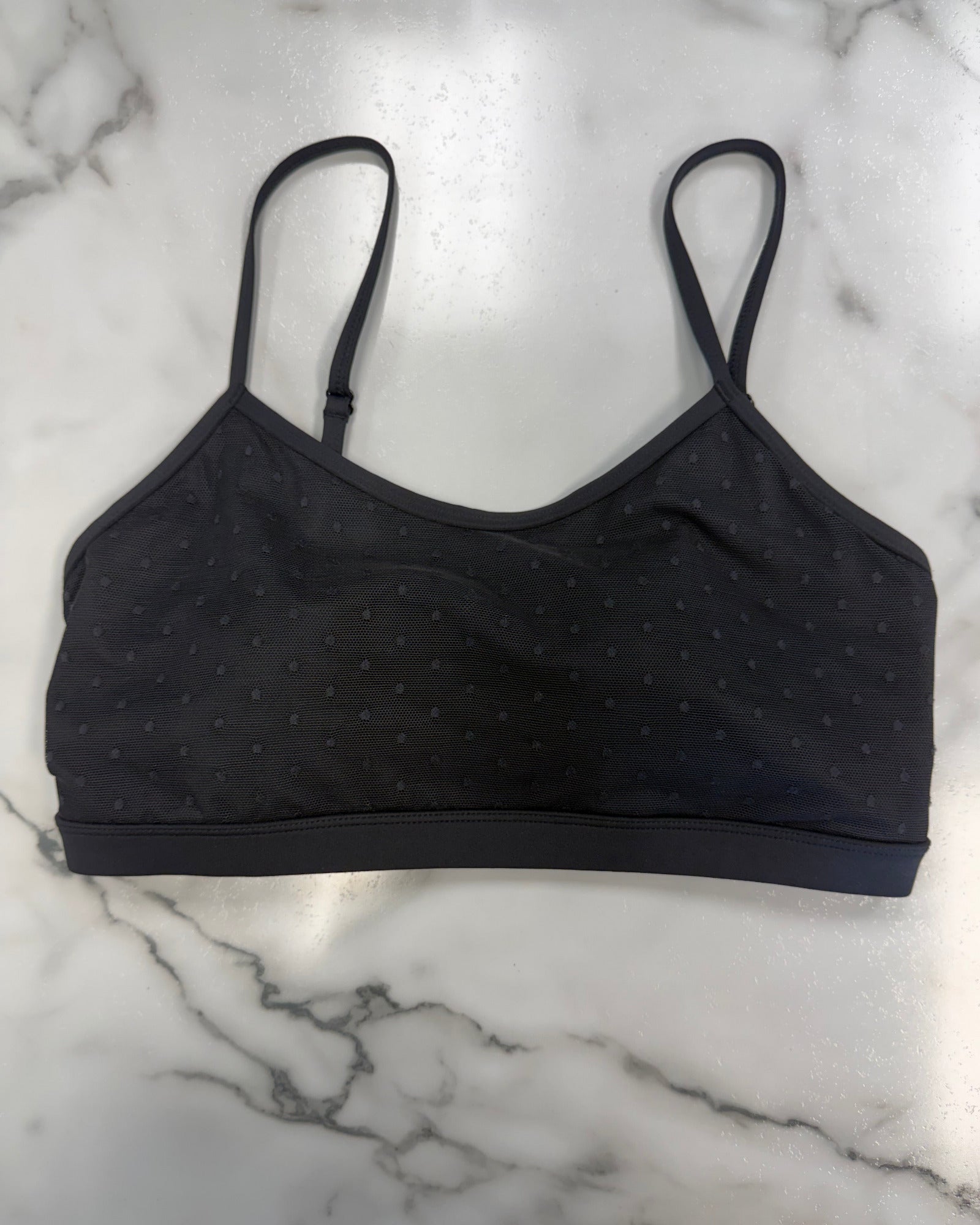 A black bra top with a subtle dotted pattern, laid flat on a white marble surface.