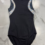 A sleeveless black one-piece leotard laid flat on a white marble surface, featuring iridescent silver and blue patterned shoulder panels.