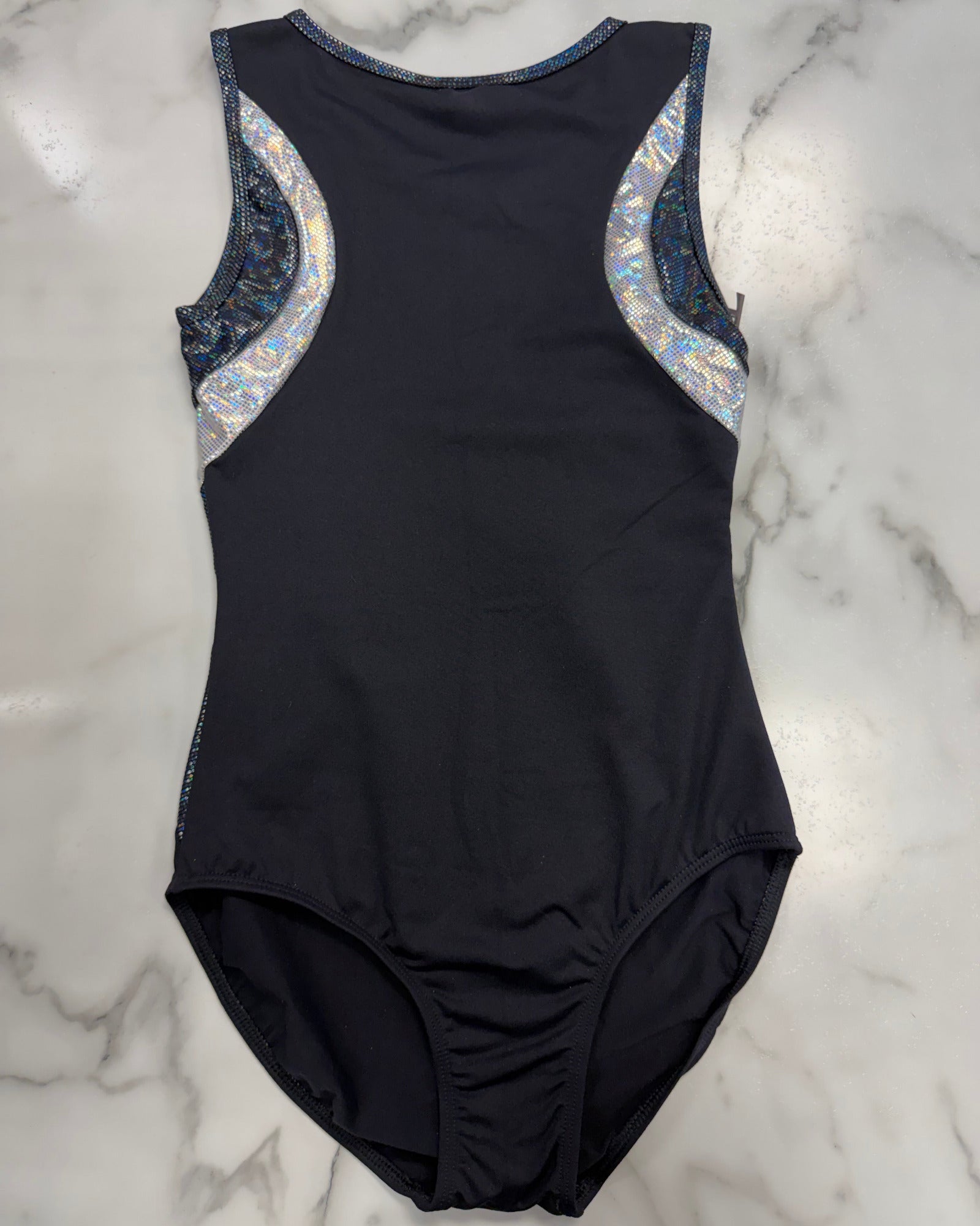 A sleeveless black one-piece leotard laid flat on a white marble surface, featuring iridescent silver and blue patterned shoulder panels.