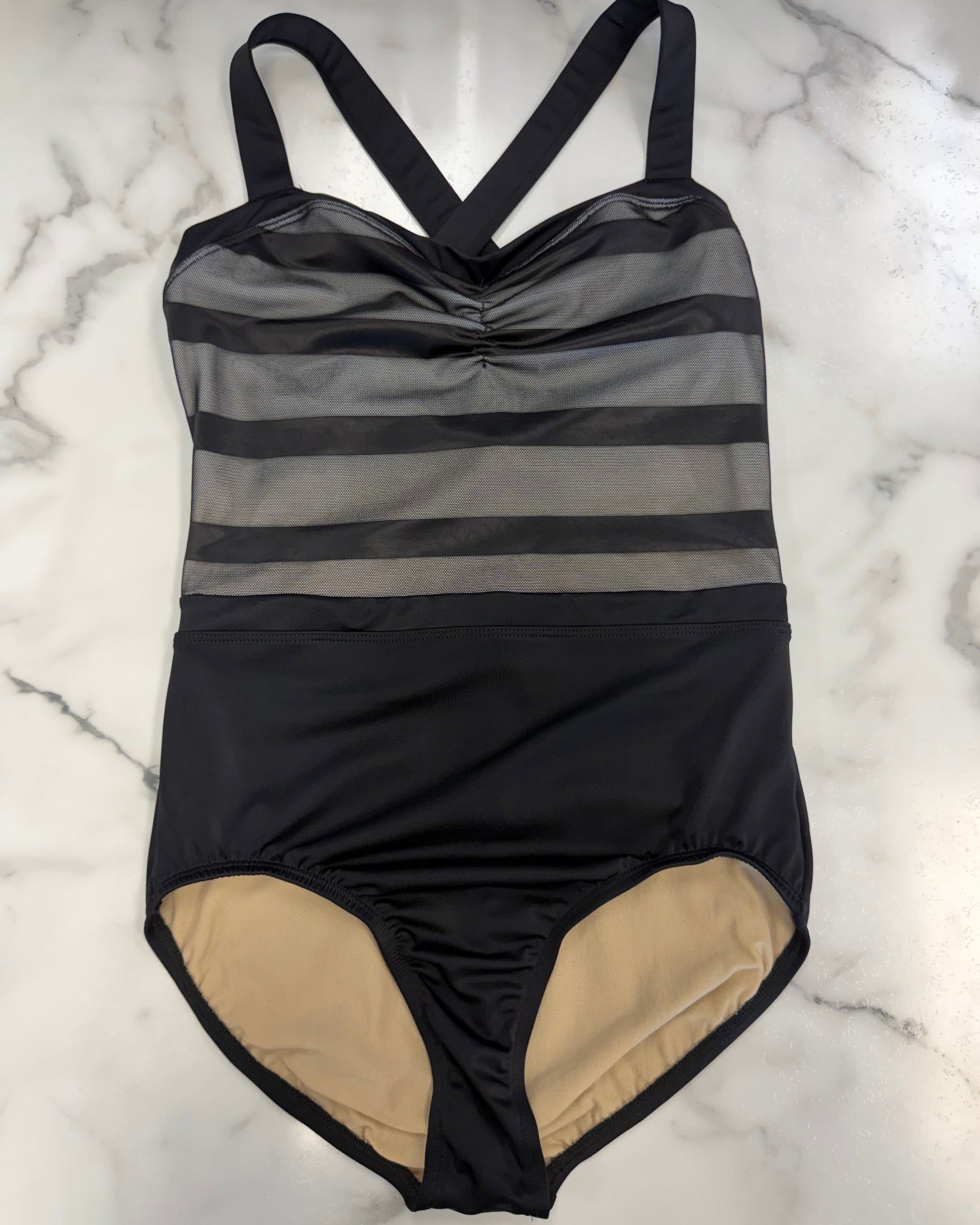 A leotard laid flat on a white marble surface. The leotard features a black and gray striped bodice with sheer horizontal mesh stripes, a ruched center, and a solid black skirt.