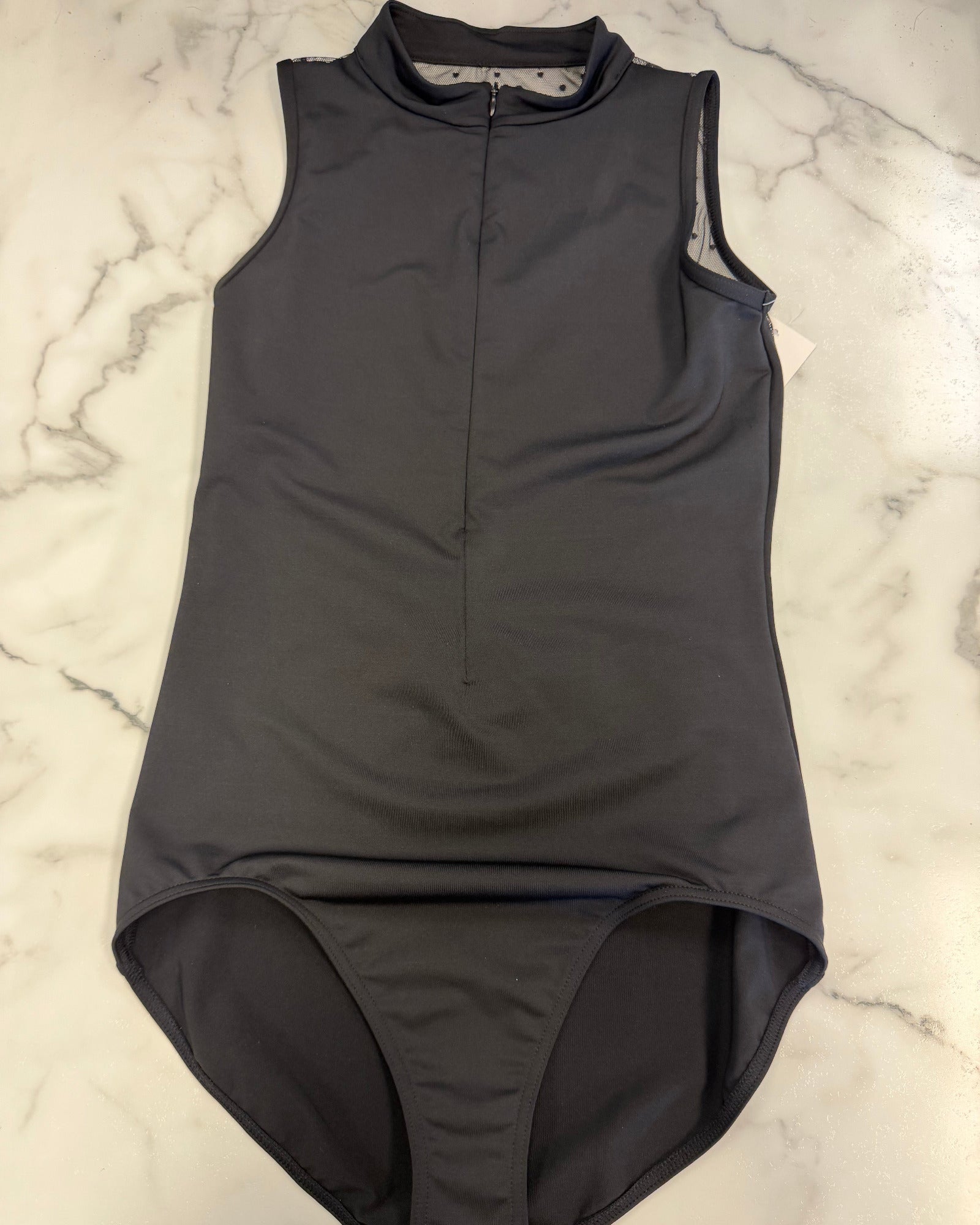 A dark black sleeveless leotard with a mock neck and front zipper, laid flat on a white marble surface.