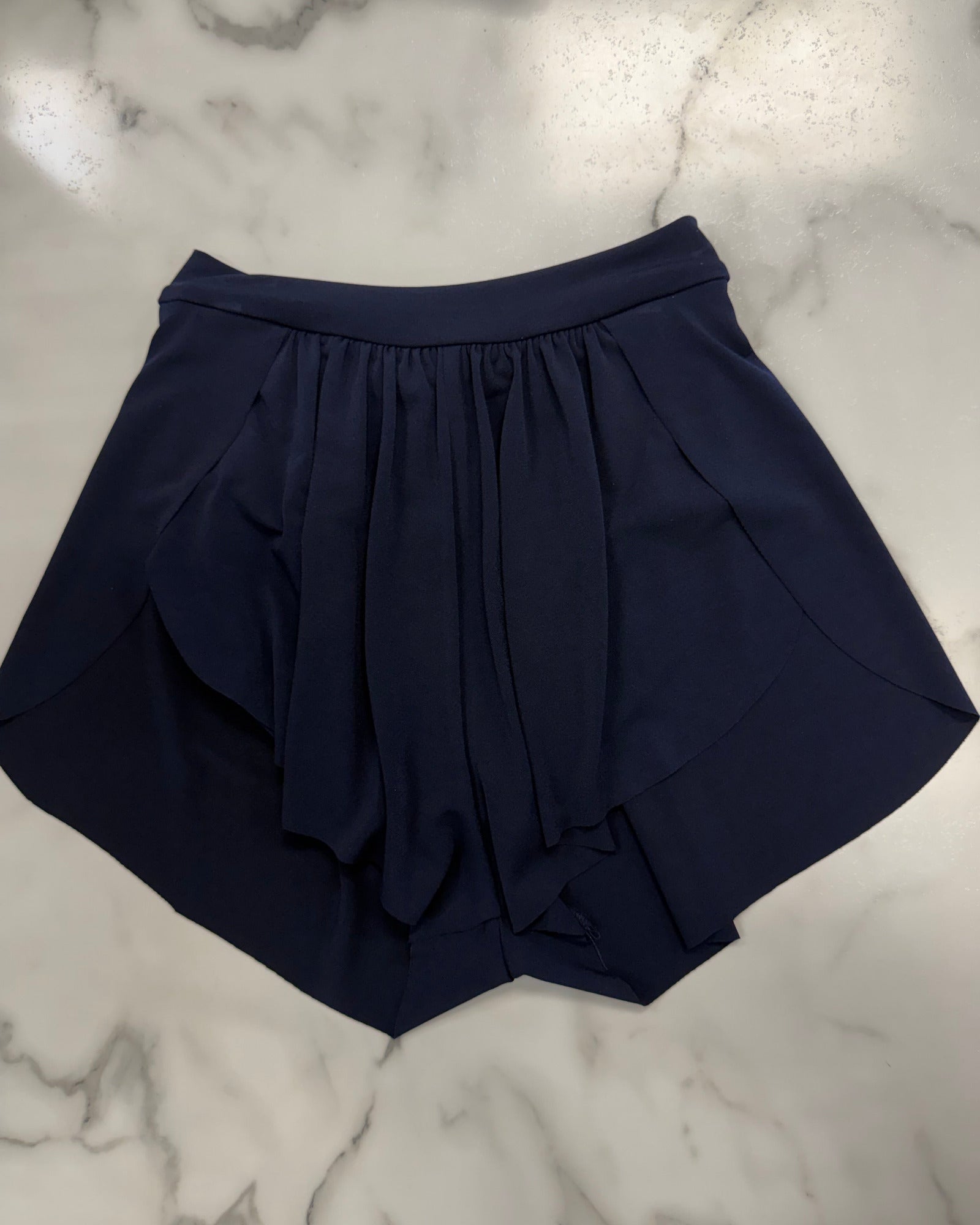 A navy blue pleated skirt with a gathered waistband, laid flat on a white and gray marble surface.
