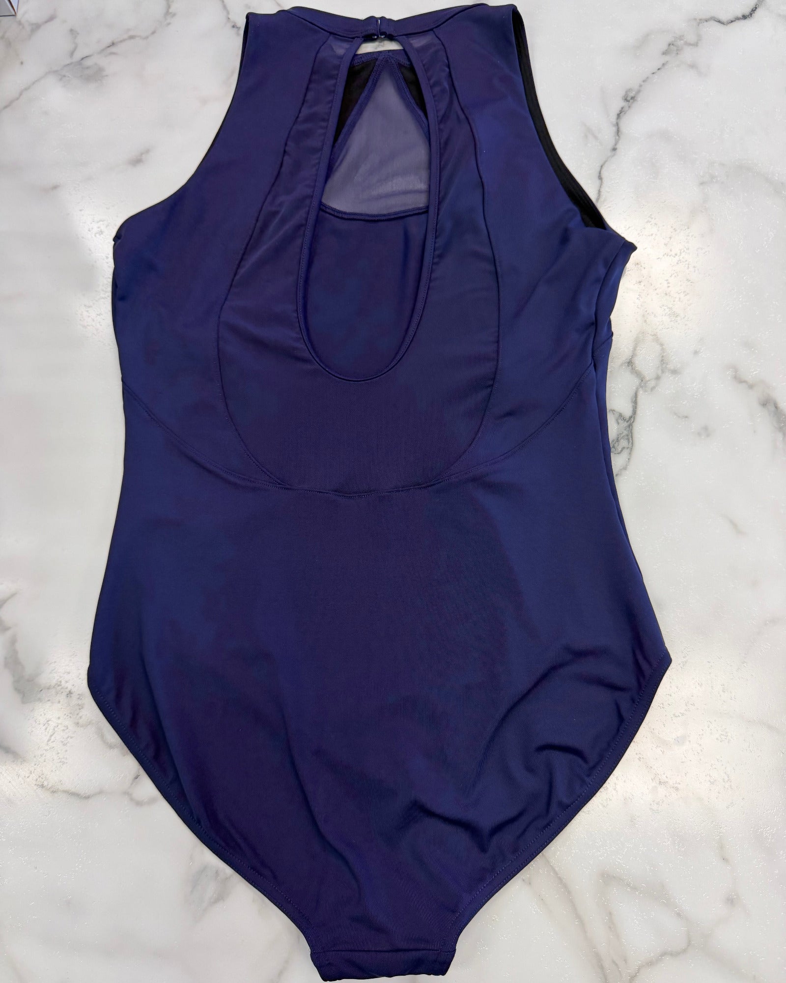 A sleeveless dark purple leotard with a keyhole back cutout, laid flat on a white and gray marble surface.