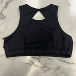 Black dance bra top shown from the back, featuring a crossover back design and wide underbust band, laid flat on a white marble surface.