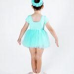 A young child viewed from the back wearing a mint green short-sleeve leotard with a matching tulle tutu skirt and a matching headband, standing on ballet slippers against a white studio background.