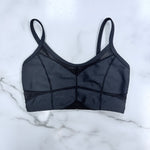 A black sports bra with structured cups and sheer mesh panels, laid flat on a white marble surface.