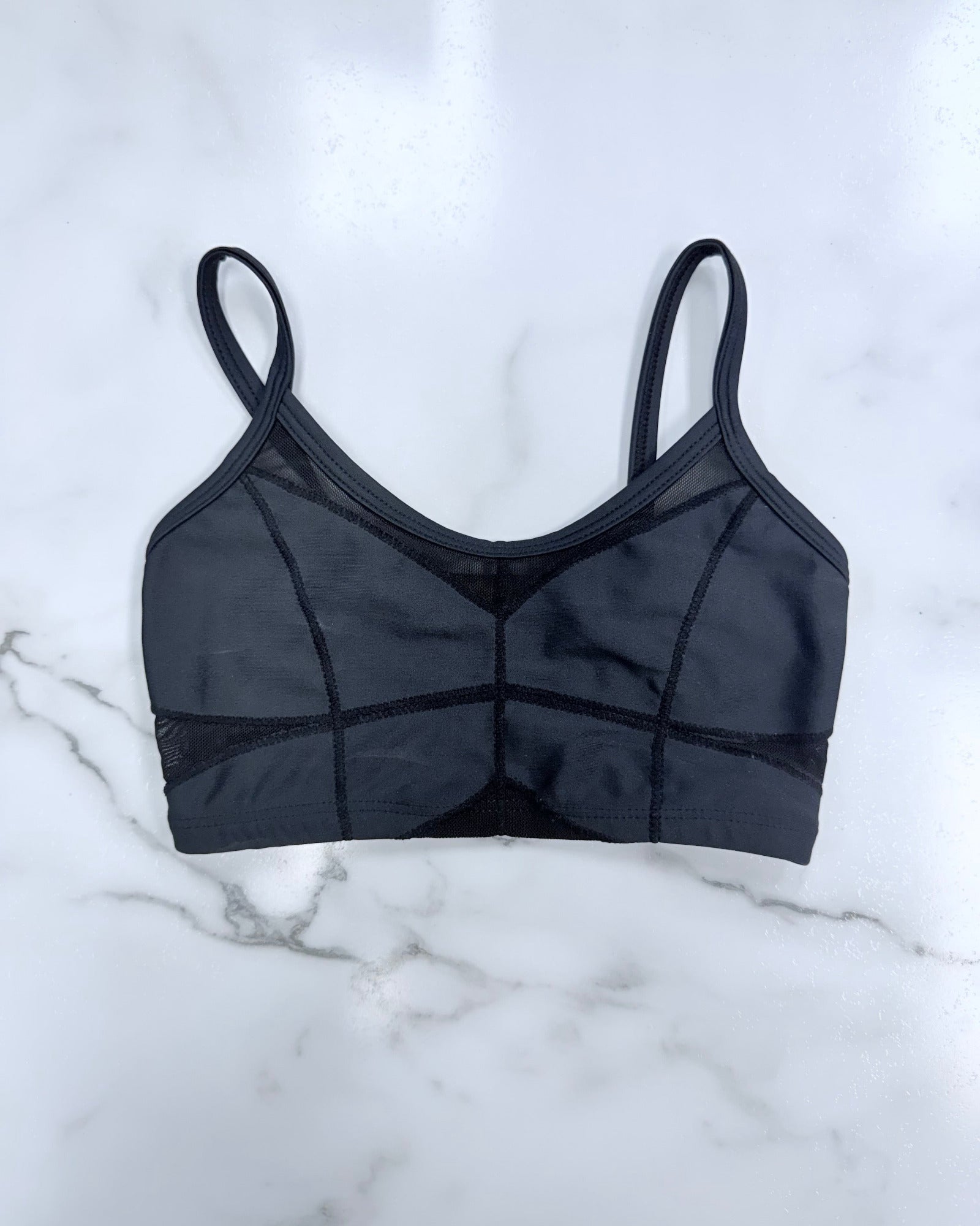 A black sports bra with structured cups and sheer mesh panels, laid flat on a white marble surface.