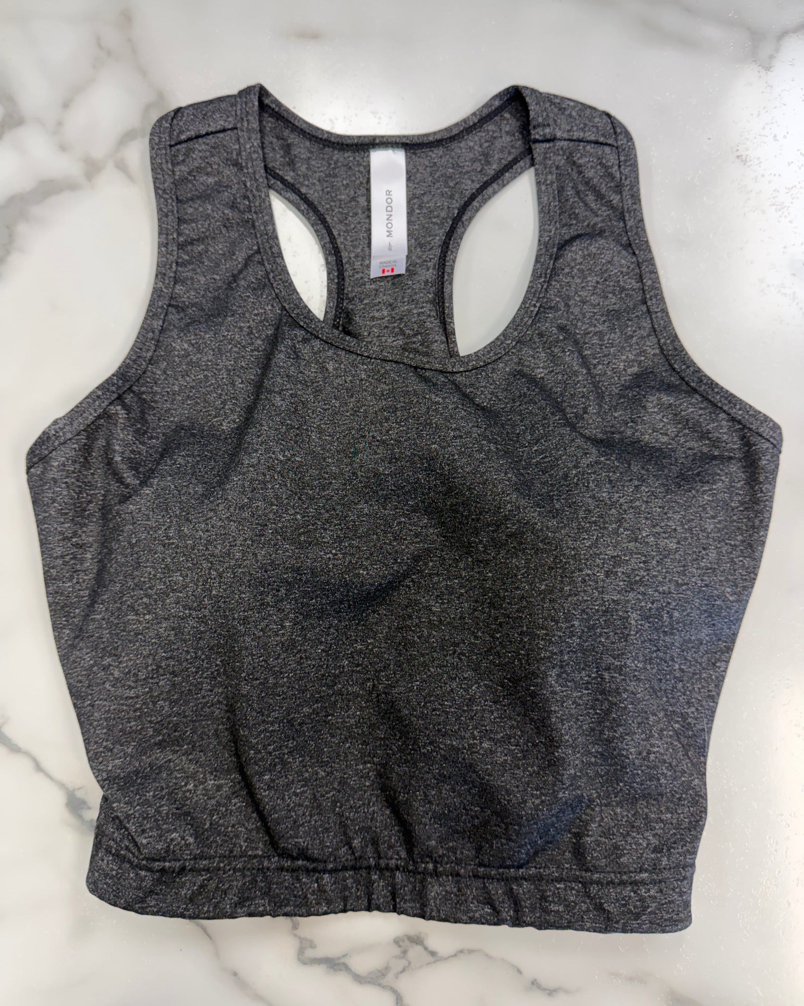 A dark heather gray racerback crop top laid flat on a white marble surface.