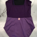 A two-tone purple leotard laid flat on a white and gray marble surface. The top portion is a dark purple, while the bottom is a lighter medium purple.