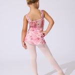 A young girl dancer shown from the back wearing a pink floral leotard, light pink tights, and ballet shoes against a plain light gray studio background.