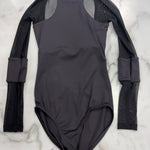 A black long-sleeve leotard with sheer mesh shoulder panels and textured black mesh sleeves, laid flat on a white marble background.