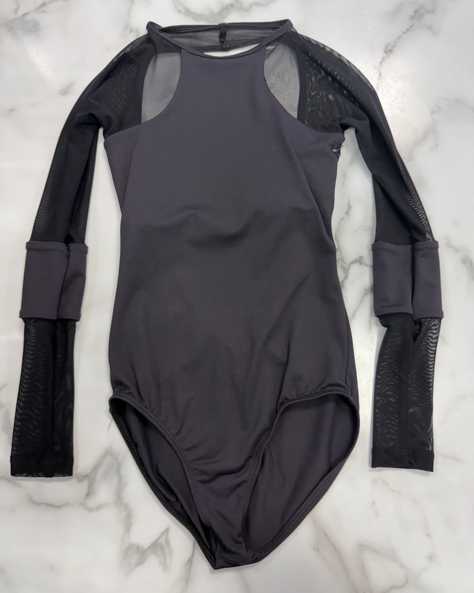 A black long-sleeve leotard with sheer mesh shoulder panels and textured black mesh sleeves, laid flat on a white marble background.