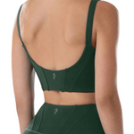 A woman shown from the back wearing a dark green dance bra and matching high-waisted leggings against a plain white background.
