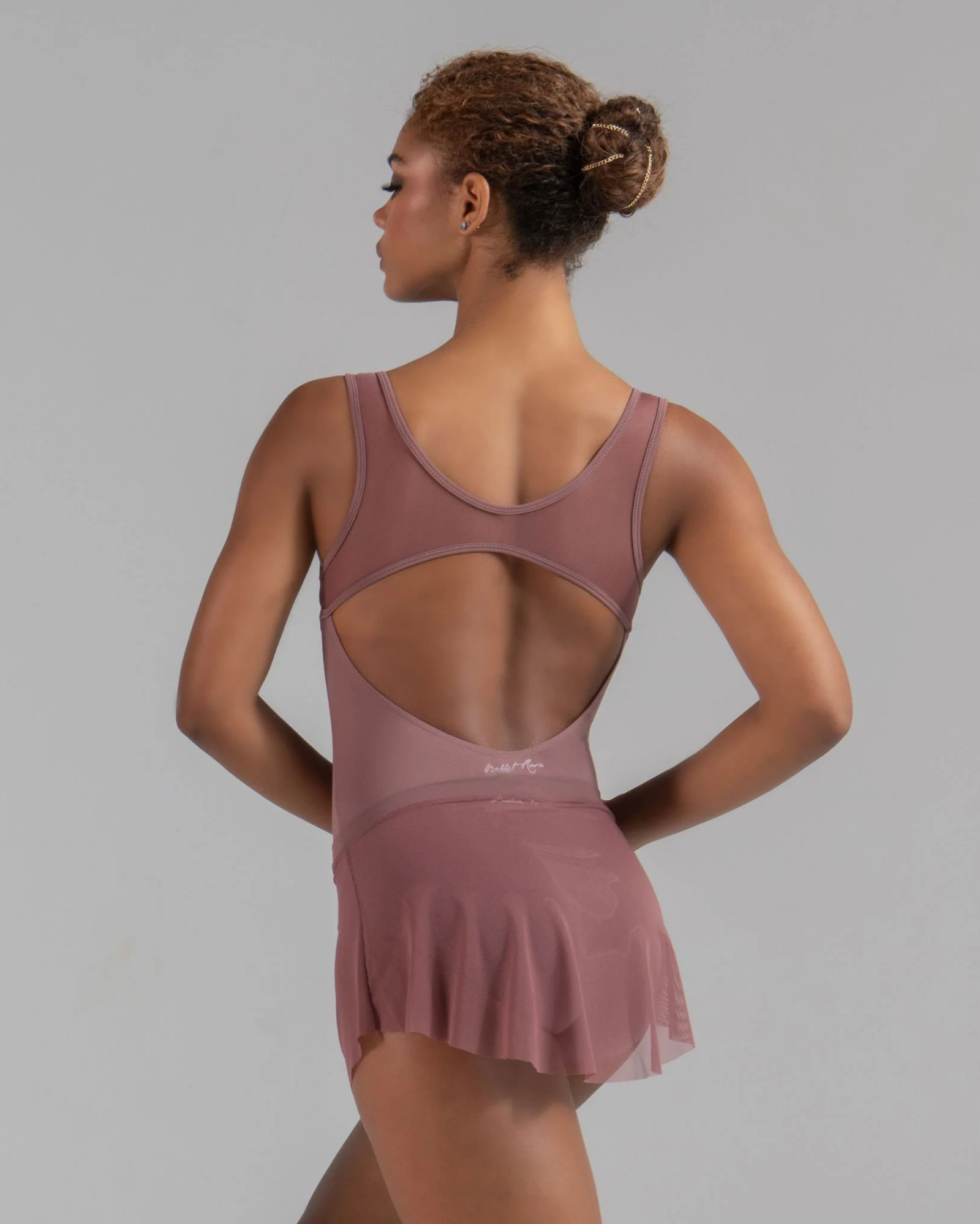 Woman wearing a mauve leotard with a skirt on a gray background