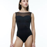 A woman modeling a black sleeveless leotard with a sheer mesh yoke and structured corset-style bodice, photographed against a clean white studio background.