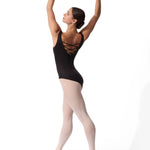 A female ballet dancer in a black leotard with criss-cross back straps, light pink tights, and pointe shoes, posed in a classical arabesque position against a solid white background.
